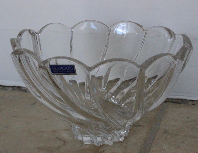 May include: A clear glass bowl with a scalloped rim and a swirl design. The bowl has a sticker on the side that says "Marquis Crystal of Austria".