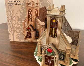 May include: A Department 56 New England Village New Britain Vestry Church ceramic building with a tall steeple, brown roof, and white snow accents. The front features double doors with a red wreath. Includes a matching product box with text.