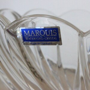 May include: A clear glass bowl with a decorative design. The bowl has a blue label that reads "Marquis by Waterford Crystal Made in Germany."