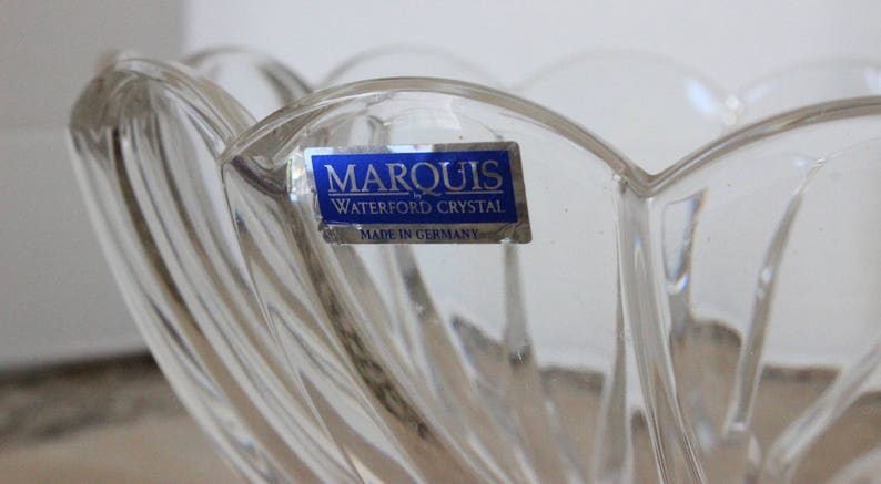 May include: A clear glass bowl with a decorative design. The bowl has a blue label that reads "Marquis by Waterford Crystal Made in Germany."