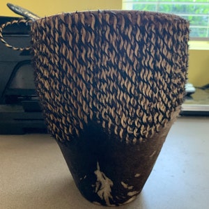 May include: A brown and white cowhide drum with a woven rim. The drum is made of natural materials and has a rustic look.