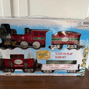 May include: A boxed Lionel North Pole Central Lines Ready-to-Play train set. The set includes a red and green engine, two carriages, and a white carriage with text. The box has a winter scene with pine trees.