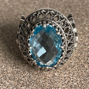 Può includere: Un anello d'argento con una grande pietra preziosa ovale di colore blu chiaro incastonata in un design a filigrana.