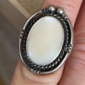 May include: A silver ring with a white oval stone set in a rope-like design. The ring has two small silver beads on the top.