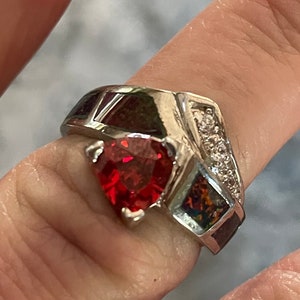 May include: A silver ring featuring a heart-shaped red gemstone, set within a band of multi-coloured stones and clear cubic zirconia.