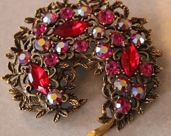 Pode incluir: Um broche dourado com um design de folhas e strass vermelhos e rosados.