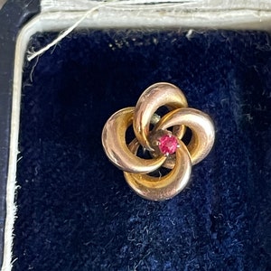 May include: A gold flower-shaped pin with a red gemstone in the center.