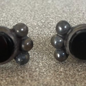 May include: A pair of silver earrings with black onyx stones. Each earring has a circular stone surrounded by five smaller silver beads.