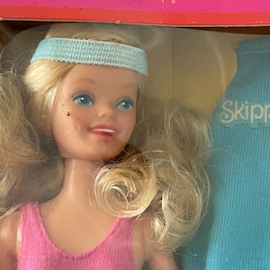 Könnte beinhalten: Eine blonde Puppe mit blauen Augen, die einen rosa Badeanzug mit dem Wort "Skipper" auf der Vorderseite trägt. Die Puppe trägt ein blaues Stirnband und hat ein hellblaues Hemd mit dem Wort "Skipper" darauf.