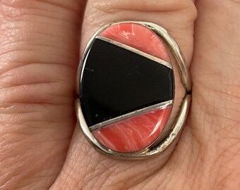 May include: A silver ring with an oval shaped stone. The stone is made of black and pink inlay.