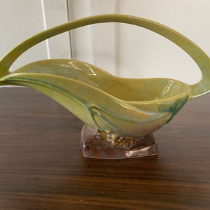 May include: A green and brown ceramic bowl with a handle. The bowl is shaped like a leaf and has a raised design of grapes on the base.