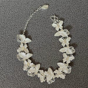 May include: Silver butterfly bracelet with delicate filigree wings. The bracelet features multiple butterfly charms connected by a chain, with a small tag near the clasp. The butterflies are detailed with a textured finish.