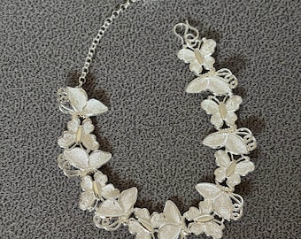 May include: Silver butterfly bracelet with delicate filigree wings. The bracelet features multiple butterfly charms connected by a chain, with a small tag near the clasp. The butterflies are detailed with a textured finish.
