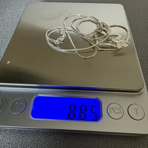 May include: A silver necklace with a butterfly pendant rests on a digital scale. The scale displays a weight of 8.85 grams. The necklace chain is a delicate snake chain style, and the butterfly pendant is detailed.