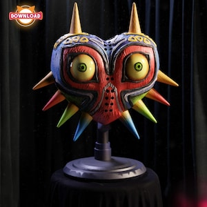 May include: A colorful, heart-shaped mask with large, yellow eyes and sharp, spiky protrusions. The mask features a red face, blue and yellow accents, and is mounted on a gray stand. The mask is a collectible item.