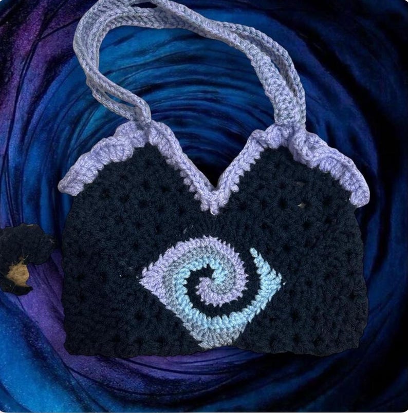 May include: Handmade crochet tote bag in navy blue with a light purple spiral design on the front. The bag has a light purple trim and handles. The background is a dark blue and purple gradient.