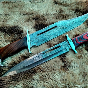May include: Two large hunting knives with ornate, etched blades and wooden handles. One handle is dark brown, the other is red and black. The blades have a turquoise hue. The knives are displayed on a textured, brown surface.