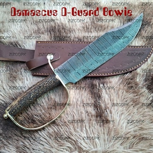 May include: Damascus D-Guard Bowie knife with a leather sheath. The blade has a unique pattern, a wooden handle, and a brass guard. The text "Damascus D-Guard Bowie" is visible.