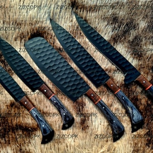 May include: An assortment of five black chef knives with textured blades and wooden handles. The handles have a dark blue and brown pattern with a red accent. The knives are arranged on a brown surface.