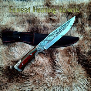 Puede incluir: Un cuchillo Forest Hunting Bowie con hoja plateada que presenta grabados de paisajes forestales, mango con segmentos de madera marrón rojiza y oscura, y virolas de metal plateado ornamentado. Incluye una funda negra con costuras rojas.