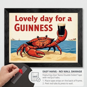 May include: Framed art print featuring a cartoon crab holding a pint of Guinness. The text "Lovely day for a Guinness" is displayed above the crab. The artwork is set on a beach with a blue ocean and a lighthouse in the background.