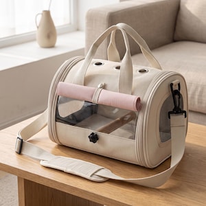 Peut inclure: Un sac de transport pour animaux de couleur beige doté d'une fenêtre rectangulaire transparente, d'un volet en tissu rose enroulable avec bouton-pression, de deux poignées supérieures et d'une bandoulière réglable avec œillets d'aération.