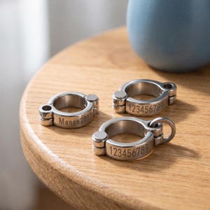 May include: Three silver-toned metal rings with a hinged, clamp-style design. One ring is engraved with the text Mango2022, while the other two rings are engraved with the numerical sequence 123456789. Each ring features a small circular attachment loop.
