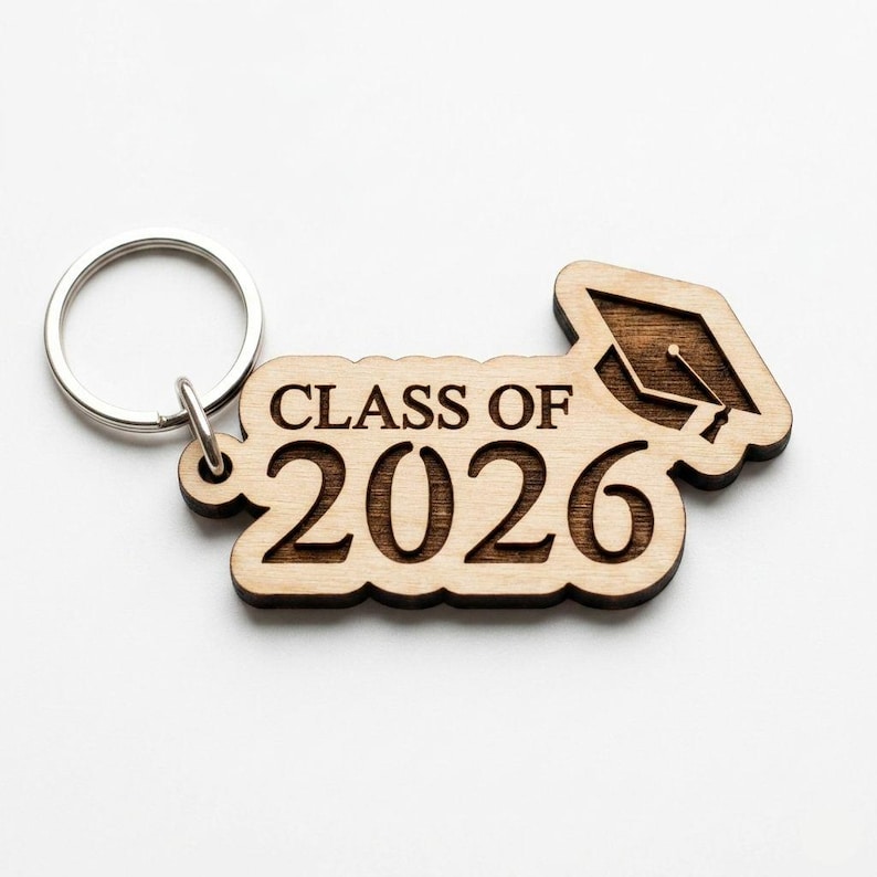 May include: Wooden keychain with the text "CLASS OF 2026" and a graduation cap design. The keychain is made of light brown wood and has a silver key ring attached. A perfect graduation gift.