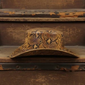 Gouden bruine cowboyhoed met pythonprint en gevlochten band.