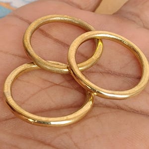 May include: Three gold-coloured rings are interlocked, displaying a warm, metallic sheen. The rings are circular, with a smooth, slightly textured surface. The image is a close-up, highlighting the rings' details and the interplay of light and shadow.