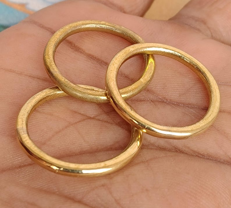 May include: Three gold-coloured rings are interlocked, displaying a warm, metallic sheen. The rings are circular, with a smooth, slightly textured surface. The image is a close-up, highlighting the rings' details and the interplay of light and shadow.