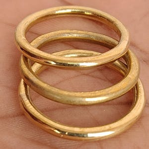 May include: Three gold-coloured rings stacked on top of each other. The rings are circular and appear to be made of metal. The rings are a warm, golden colour and have a slightly worn appearance.
