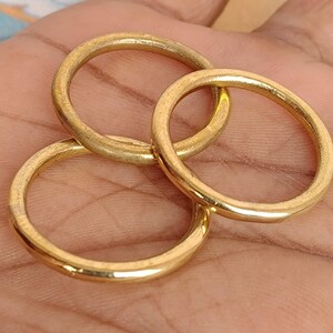 May include: Three gold-coloured rings are interlocked, displaying a warm, metallic sheen. The rings are circular, with a smooth, slightly textured surface. The image is a close-up, highlighting the rings' details and the interplay of light and shadow.