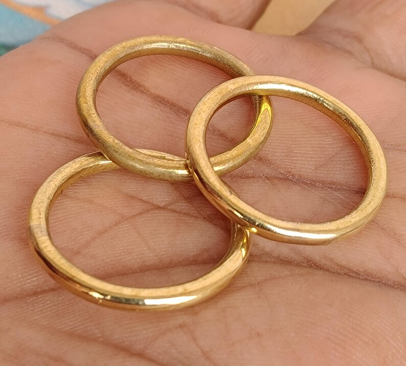 May include: Three gold-coloured rings are interlocked, displaying a warm, metallic sheen. The rings are circular, with a smooth, slightly textured surface. The image is a close-up, highlighting the rings' details and the interplay of light and shadow.
