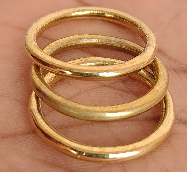 May include: Three gold-coloured rings stacked. The rings are circular and appear to be made of metal. The rings are a warm, golden colour and have a slightly worn appearance.