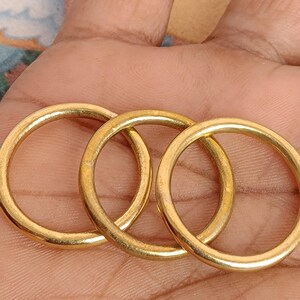 May include: Three gold-coloured metal rings are interlocked, forming a chain-like pattern. The rings are circular with a smooth, polished surface, reflecting light. The image is a close-up, highlighting the details of the metalwork.