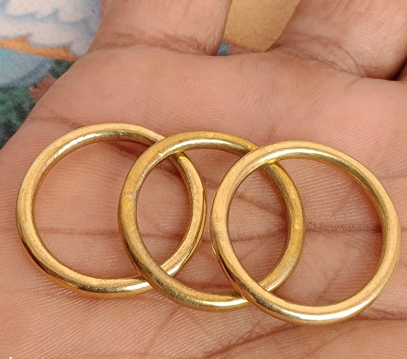 May include: Three gold-coloured metal rings are interlocked, forming a chain-like pattern. The rings are circular with a smooth, polished surface, reflecting light. The image is a close-up, highlighting the details of the metalwork.