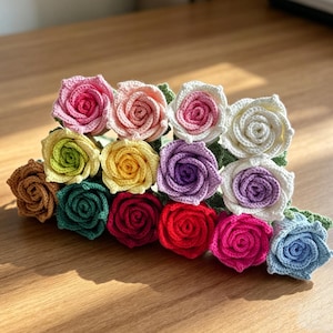 Könnte beinhalten: Eine Sammlung von fünfzehn einzelnen gehäkelten Rosen in verschiedenen Farben, darunter Rosa, Pfirsich, Weiß, Gelb, Violett, Braun, Dunkelgrün, Rot, Magenta und Hellblau, jeweils mit detaillierten Blütenblättern und grünen Blättern.