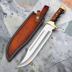 May include: A fixed-blade knife with a polished steel blade, a dark wood handle, and brass accents. The knife is accompanied by a tan leather sheath featuring intricate floral tooling, white stitching, and a brass snap button closure.