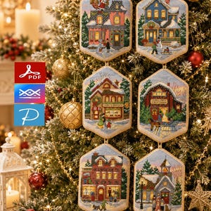 May include: Six hexagonal cross-stitch ornaments featuring detailed winter village scenes, including a bakery, a toy shop, and a tree farm. Each piece is finished with a gold-toned border and a hanging loop, displaying intricate embroidery work.