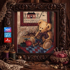 May include: A framed cross-stitch sampler featuring a teddy bear with a smaller bear, an apple, and a house. The sampler has an alphabet and a house design. The frame is dark brown and ornate. The image includes sewing notions.