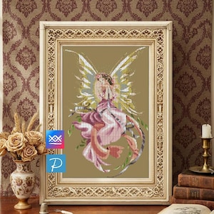 May include: A framed cross-stitch artwork featuring a fairy with flowing pink and white dress, floral crown, and large, detailed wings. The fairy is surrounded by green vines. The frame is ornate, gold-colored, and the background is a warm, neutral tone.