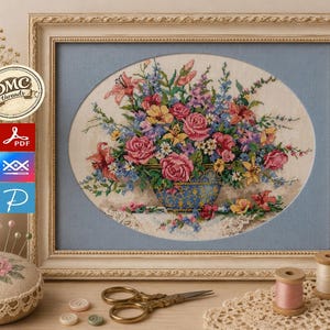 Puede incluir: Un bordado en punto de cruz enmarcado que representa un ramo de flores colorido en un jarrón azul y dorado. La obra está colocada en un paspartú ovalado y un marco color crema. La imagen incluye iconos de hilos DMC, PDF y patrón.