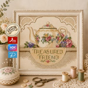 Puede incluir: Un patrón de punto de cruz enmarcado que muestra una tetera floral y el texto "TREASURED FRIEND" con un pequeño corazón. El diseño incluye flores rosas y moradas, dentro de un marco claro, acompañado de artículos de costura como carretes.