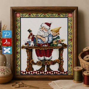 Puede incluir: Un bordado en punto de cruz enmarcado que representa a Santa Claus pintando un soldado de juguete en un banco de trabajo de madera, acompañado por un elfo con una paleta de pintura. El diseño tiene un borde floral en un marco de madera oscura.