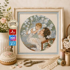 Könnte beinhalten: Eine gerahmte Kreuzstichstickerei, die eine Person mit einem Baby umgeben von weißen Blumen zeigt. Das Kunstwerk befindet sich in einem hellen Holzrahmen. Daneben liegen Nähutensilien wie ein Nadelkissen, eine Schere und Garnrollen.