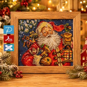 Puede incluir: Un bordado enmarcado que representa a Papá Noel con un traje rojo, sosteniendo una linterna y regalos. La obra de arte está ambientada sobre un fondo azul con efecto de nieve. El marco es de madera marrón claro. Tema navideño.