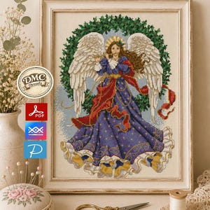 May include: A framed cross-stitch pattern featuring an angel with large white wings playing a flute, wearing a long purple dress with gold star accents and a red sash, centered in front of a green holly wreath, displayed in a light wood frame.