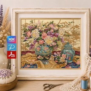 Könnte beinhalten: Ein gerahmtes Kreuzstichbild eines Blumenstilllebens mit einer großen Vase voller bunter Blumen. Das Kunstwerk umfasst eine kleinere Vase und eine Schale, alles vor einem gemusterten Hintergrund. Der Rahmen ist weiß.