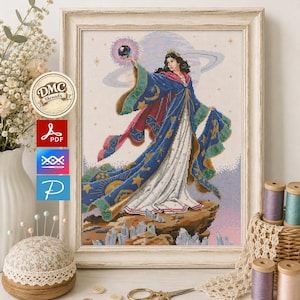 Puede incluir: Un patrón de punto de cruz enmarcado que muestra una figura con un vestido largo azul y blanco sosteniendo un orbe oscuro. El diseño incluye motivos celestiales como estrellas y lunas, sobre un fondo de un planeta y un paisaje rocoso con cristales.
